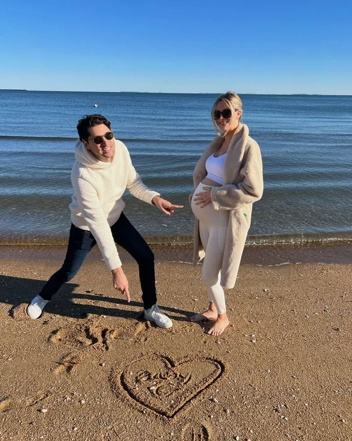 Elizabeth and Sacha on a beach beside a heart drawn in the sand
